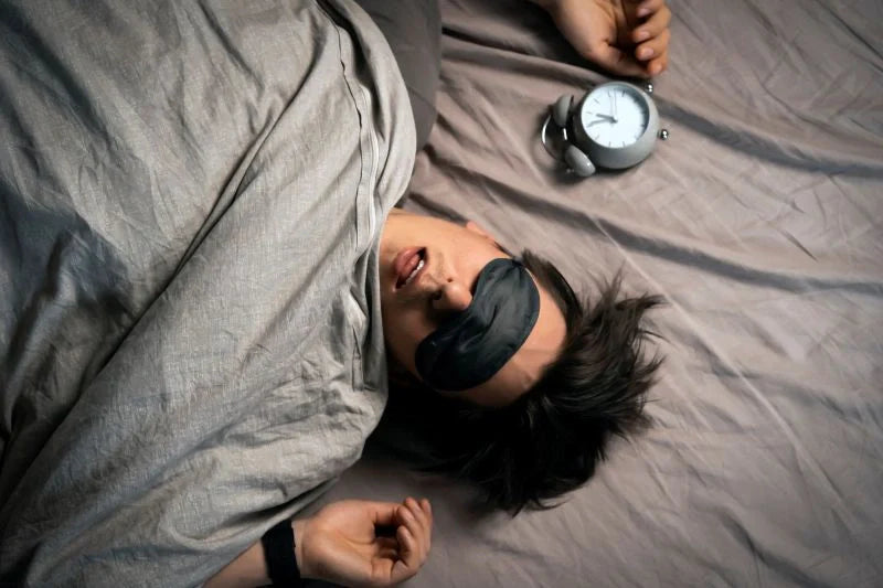 A person wearing a sleep mask, surrounded by a calming atmosphere, demonstrating how melatonin sleep support can promote restful sleep in a quiet, dark environment.