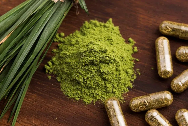 Green powder supplement and capsules next to fresh green herbs, showcasing detox drinks ingredients known for their cleansing properties.