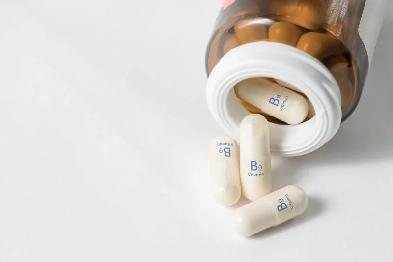 A bottle of Vitamin B9 supplements spilling onto a white surface, highlighting the advantages of Vitamin B Complex for overall health.